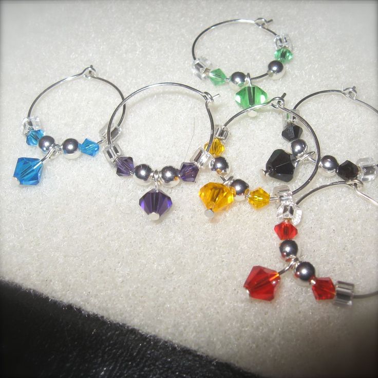 four pairs of wine glass charms with swarong beads on them sitting on a white cloth