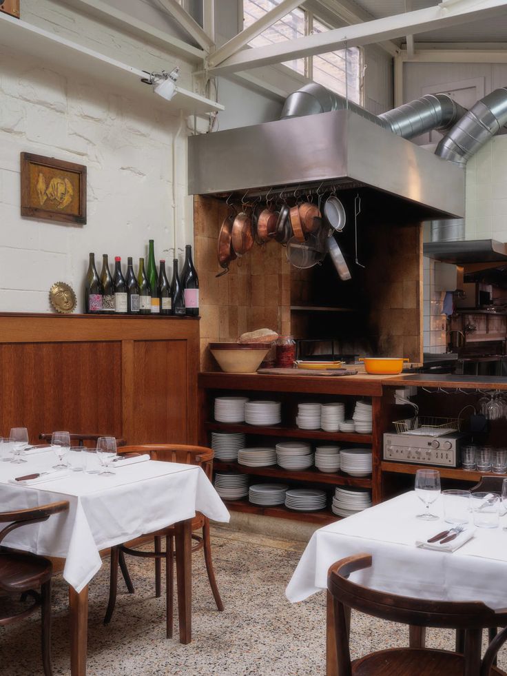 an empty restaurant with tables and chairs in front of the stove, pots and pans hanging from the ceiling