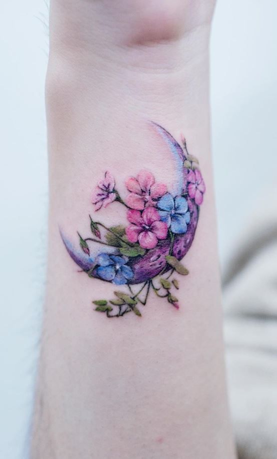 a woman's wrist tattoo with flowers and a crescent shaped moon on the side