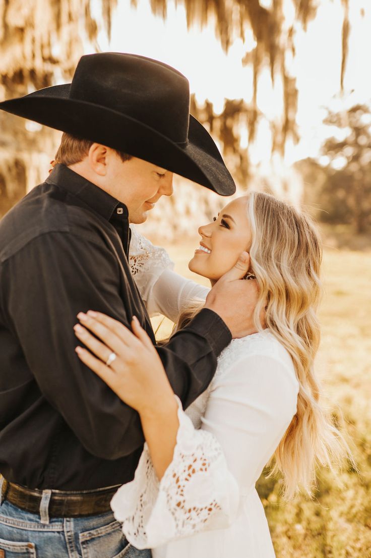 a man in a cowboy hat hugging a woman's face while she is wearing a white shirt and jeans