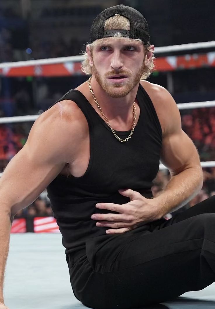 a man sitting on the ground in front of a wrestling ring with his hands on his hips