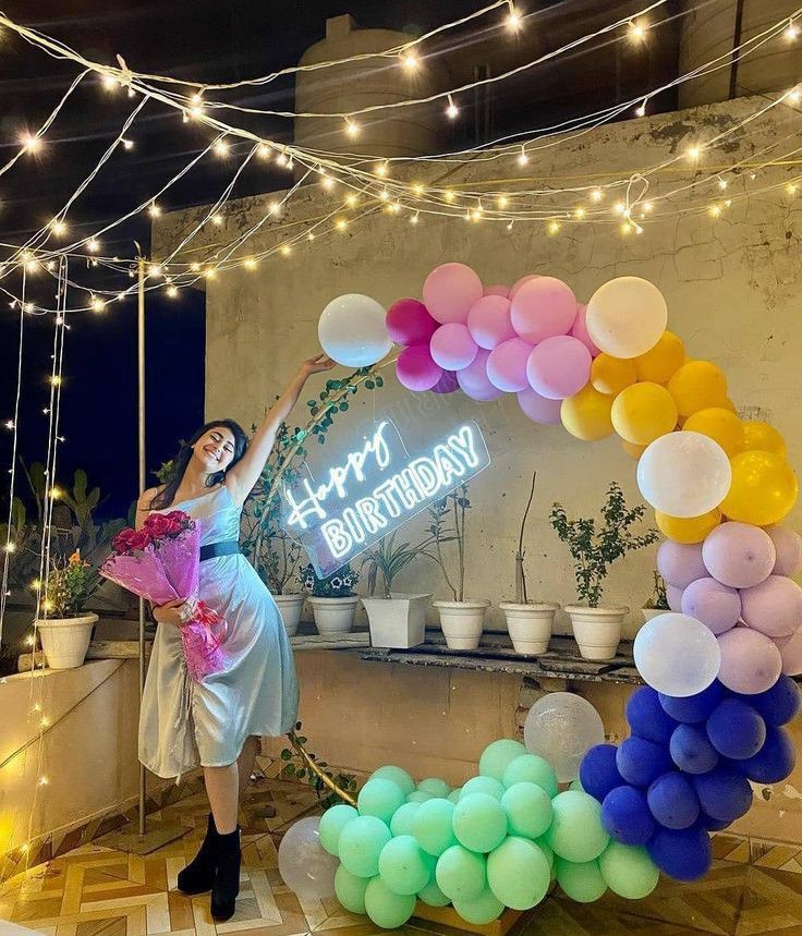 a woman standing in front of a birthday arch with balloons