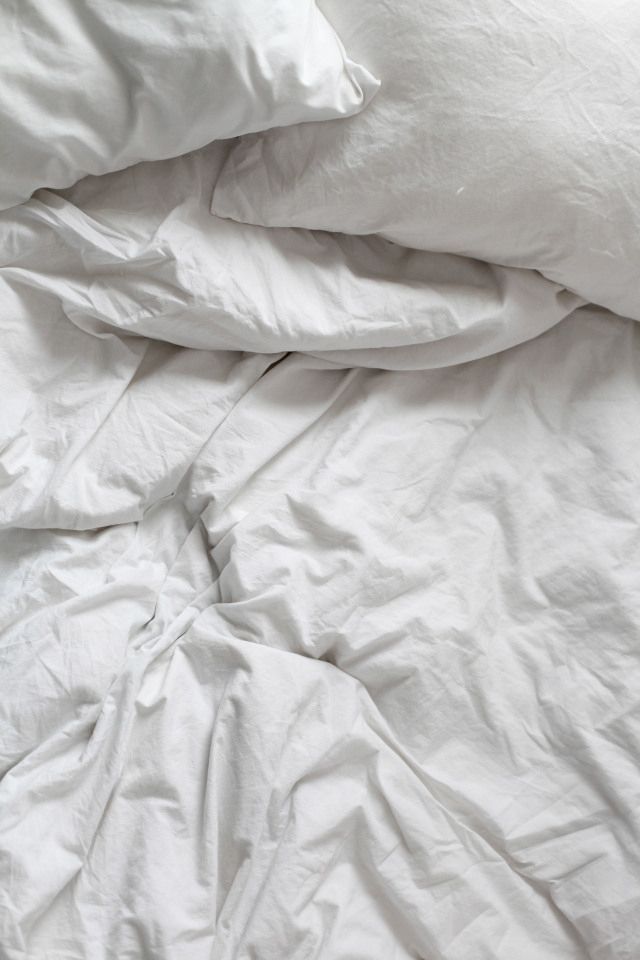 an unmade bed with white sheets and pillows