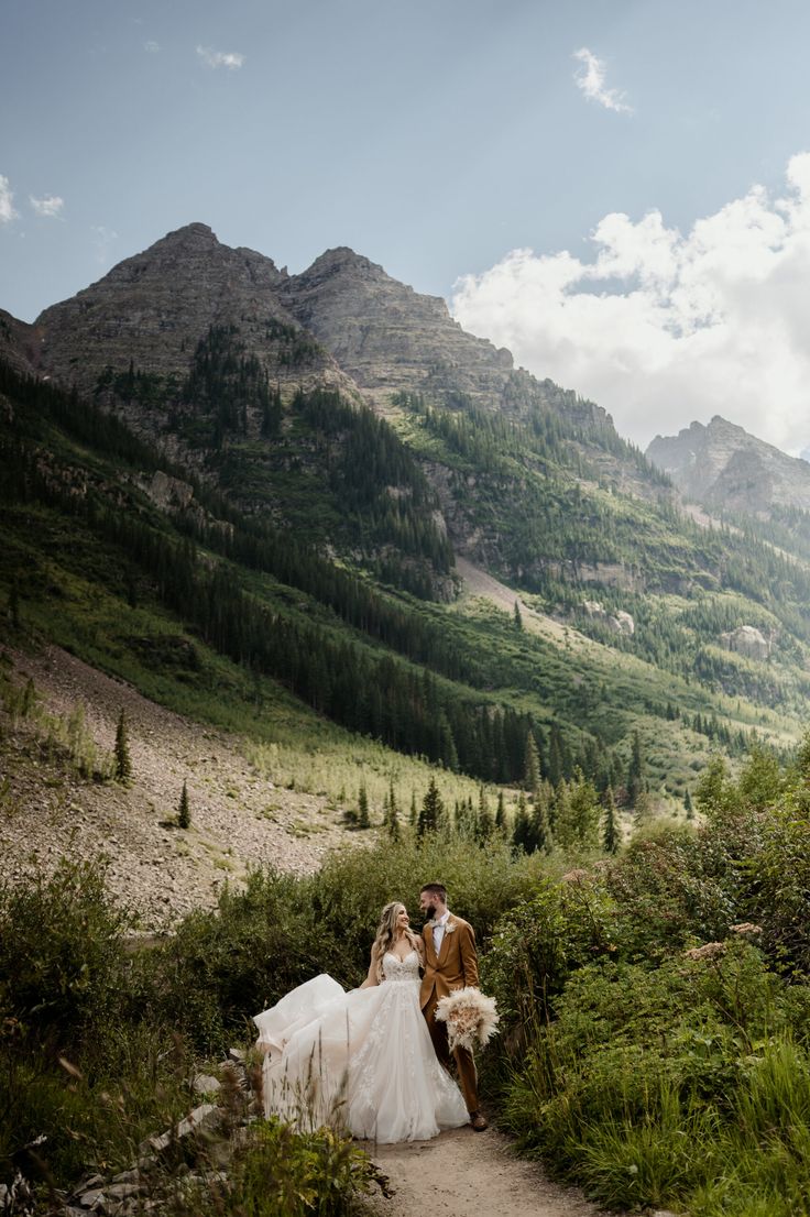 a bride and groom are sitting on a path in the mountains with their pet dog