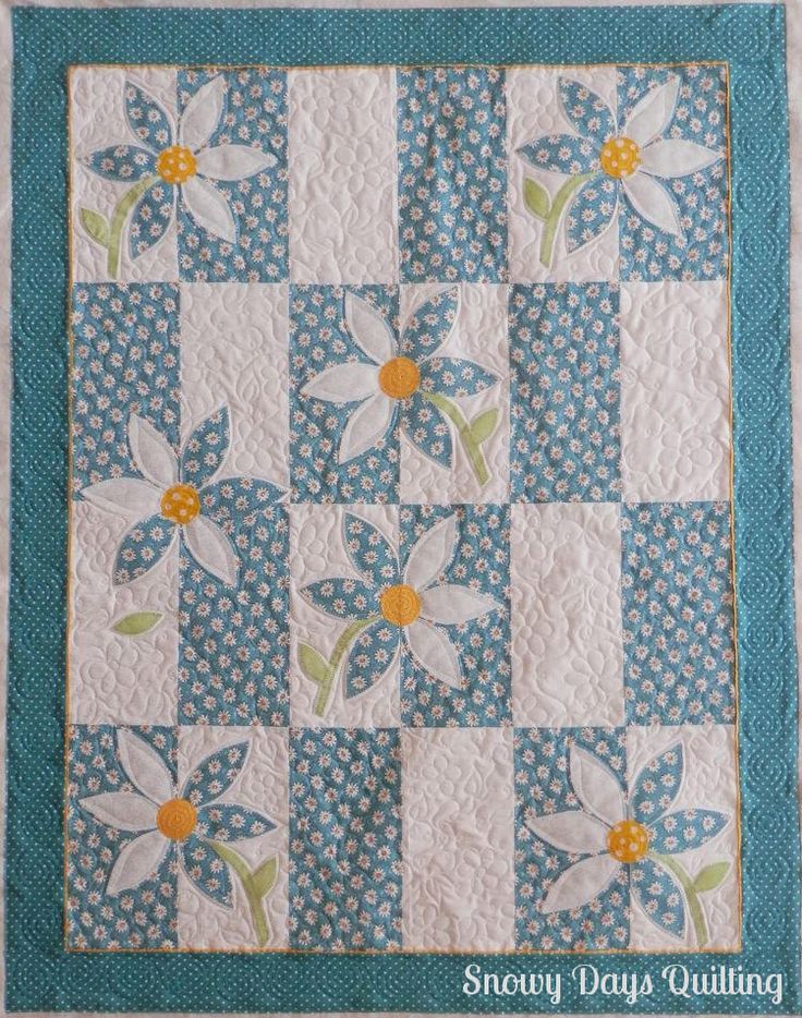 a blue and white quilted wall hanging with daisies on the center, along with two yellow centers