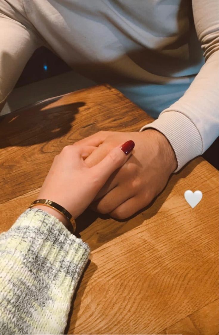 two people holding hands on top of a wooden table in front of a heart shaped object