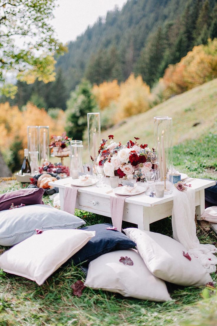 a table with pillows and flowers on it in the middle of a grassy area next to trees