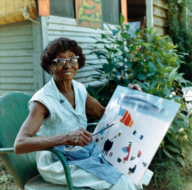 an older woman sitting on a chair holding a painting