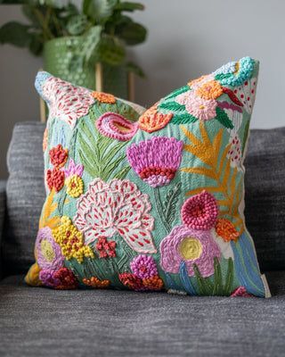 a colorful pillow sitting on top of a gray couch next to a potted plant