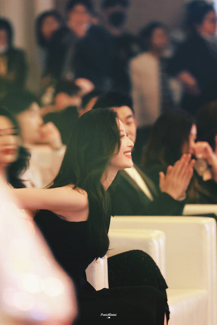 a woman sitting in front of a group of people at an event with their hands up