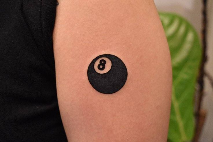 a person with a tattoo on their arm has a pool ball in the shape of a 8 - ball