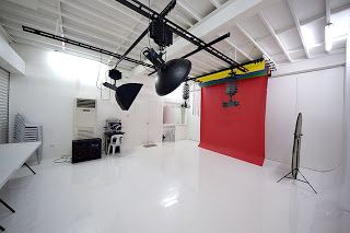 an empty room with white floors and black lights hanging from the ceiling in front of a red wall