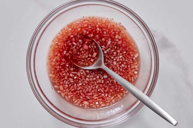 a glass bowl filled with red food and a spoon on top of it next to a white table