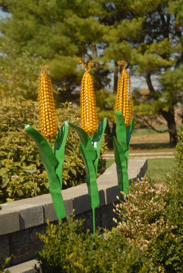 three fake corn on the cob are in front of some bushes