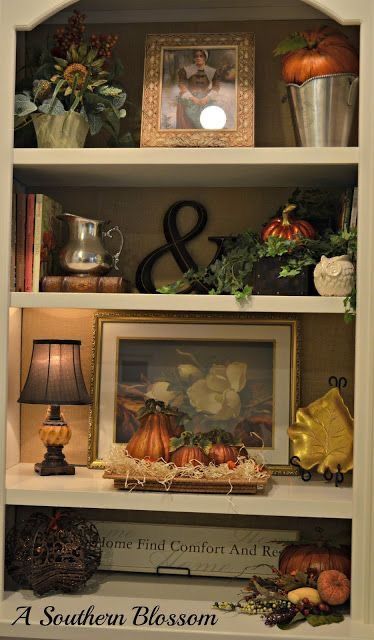 a white book shelf with pumpkins and other items on it, including a lamp