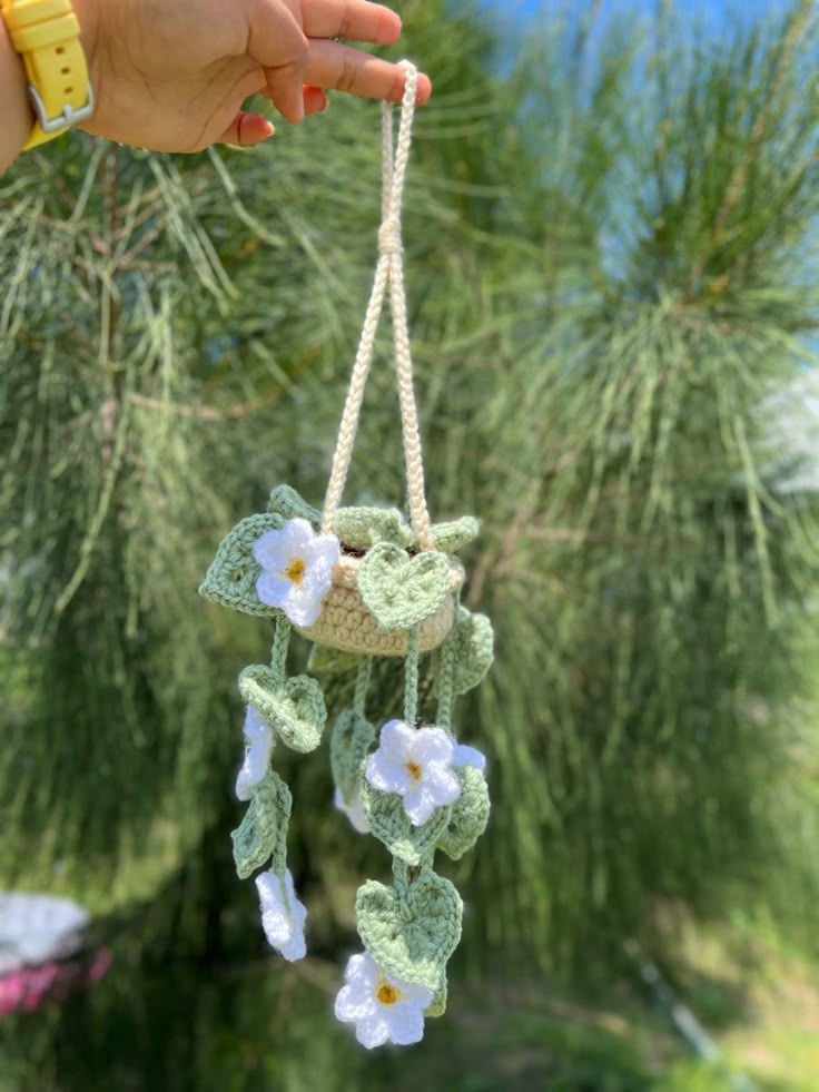 a hand holding a small crocheted mobile with flowers hanging from it's side