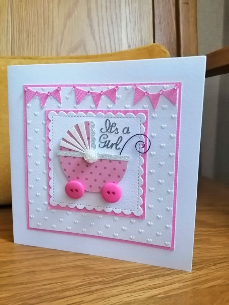 a pink and white card with a baby carriage on it's front, sitting on a wooden table