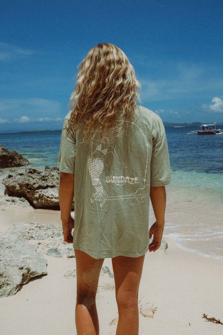 Model at the beach wearing a sun hat and showing the back of her t-shirt, a sage green t-shirt with mermaid illustration Surf Suit, Cheeky Bikinis, Large Bust, Measurement Length, The Outdoors, Positive Vibes, Oversized Fits, Sage Green, Unisex T Shirt