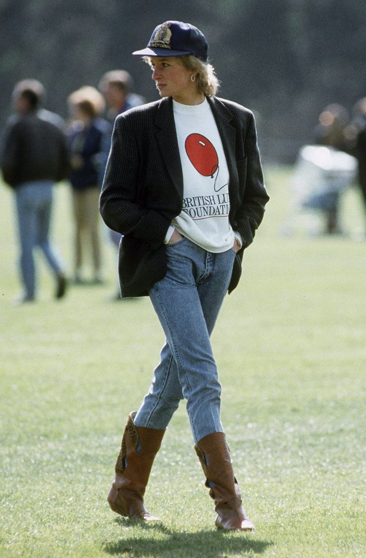 a woman walking across a lush green field wearing cowboy boots and a t - shirt