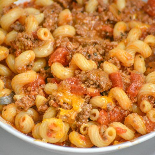 a white bowl filled with pasta and meat in tomato sauce on top of a table