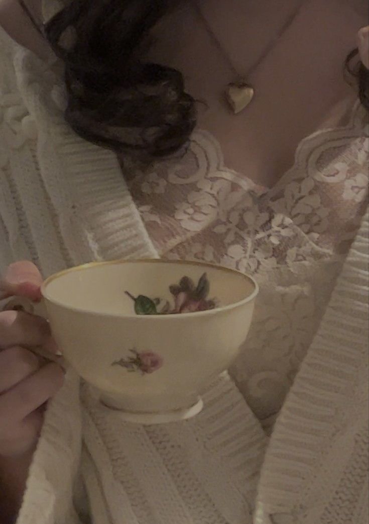 a woman is holding a white bowl with flowers on it while wearing a lace sweater