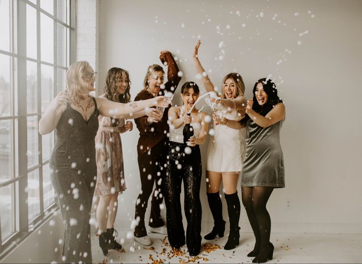 a group of women standing next to each other in front of a window with confetti