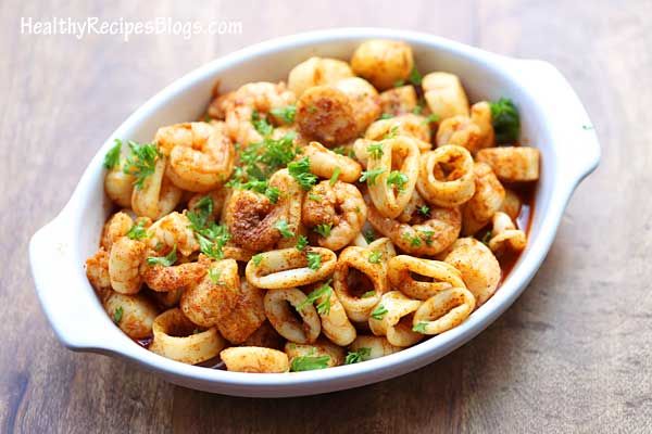 a white bowl filled with pasta and meat on top of a wooden table next to a fork