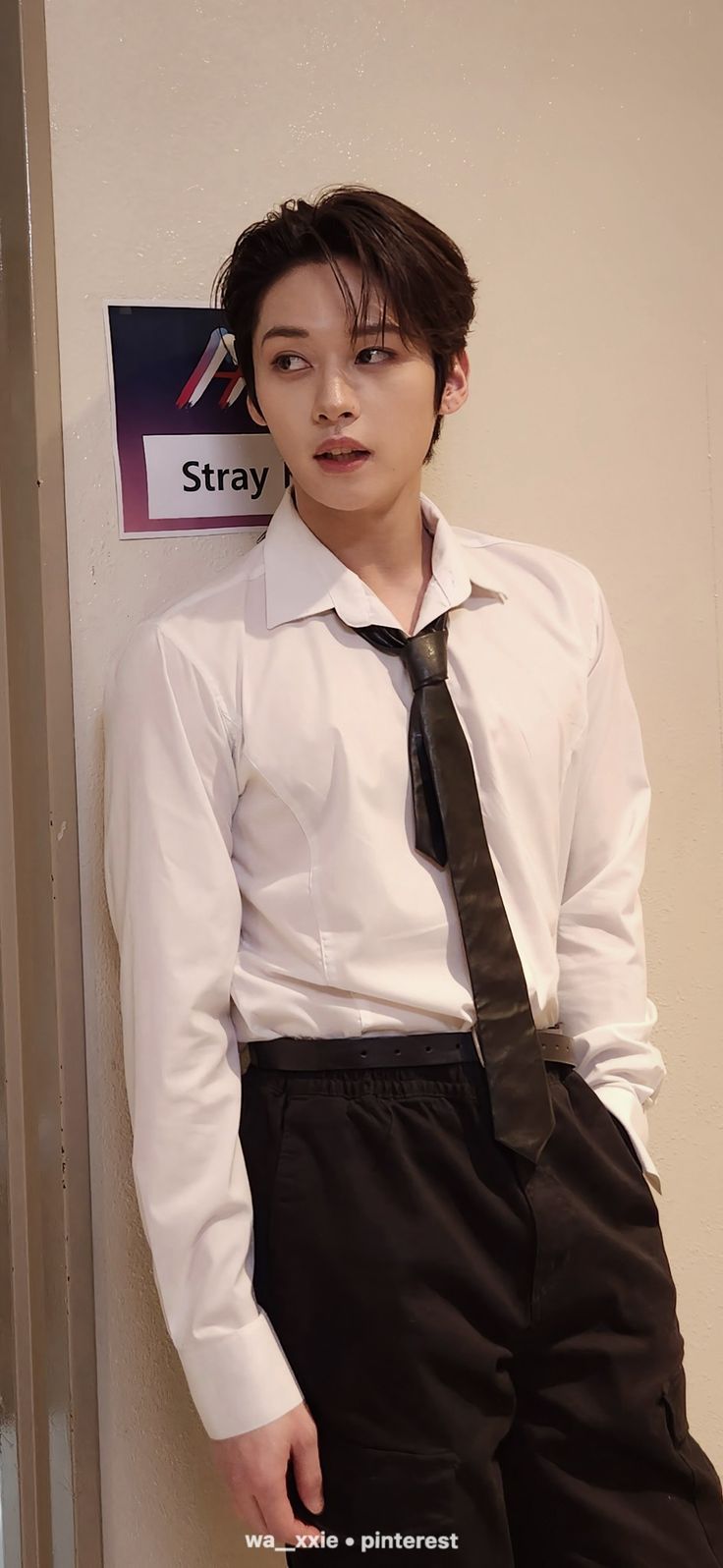 a young man in a white shirt and tie leaning against a wall with his hands on his hips