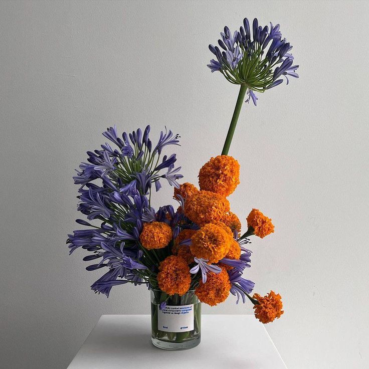 a vase filled with purple and orange flowers on top of a white table next to a wall