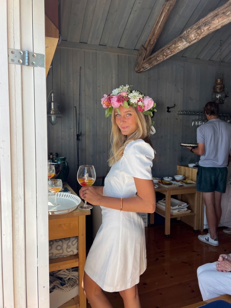 a woman in a white dress holding a glass of wine and wearing a flower crown