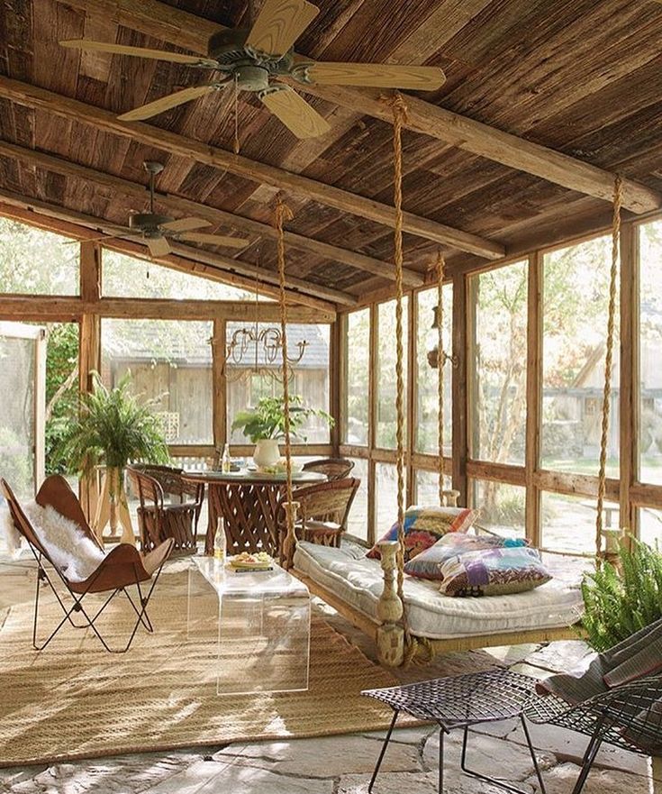 a porch with chairs, tables and a hanging bed in the middle is covered by wood planks