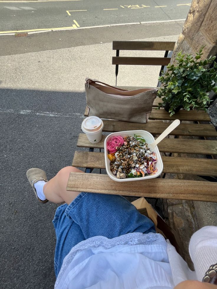 a person sitting on a wooden bench with a bowl of food in front of them