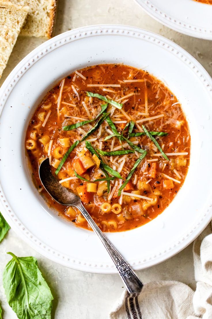 two bowls of pasta soup with bread on the side