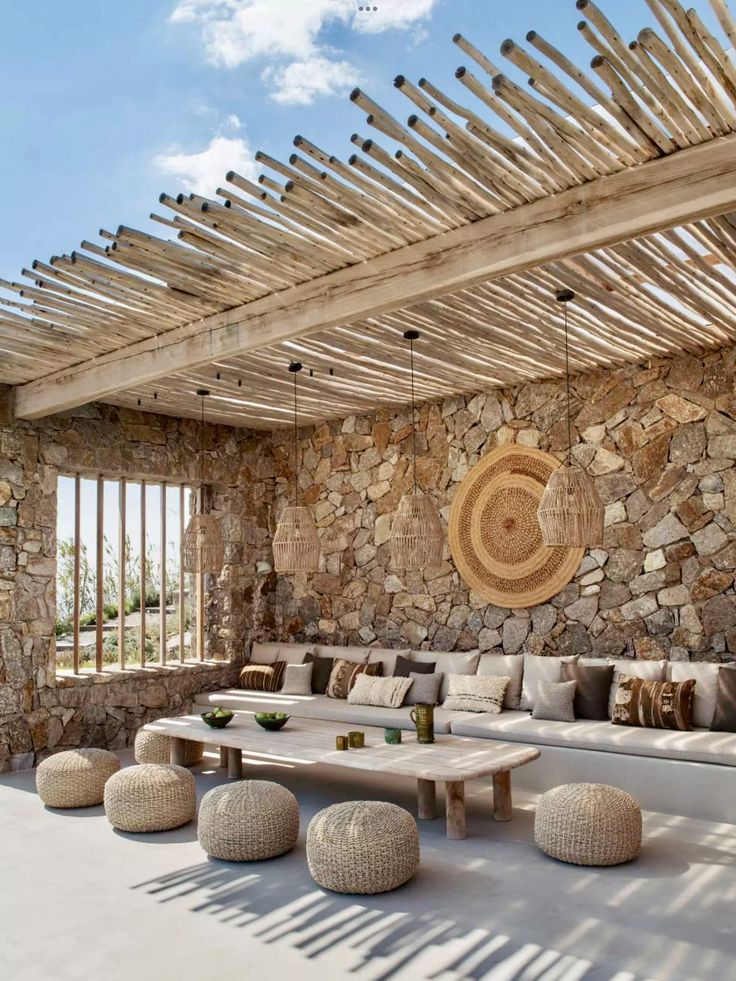 an outdoor living room with stone walls and wooden beams on the ceiling, surrounded by white furniture