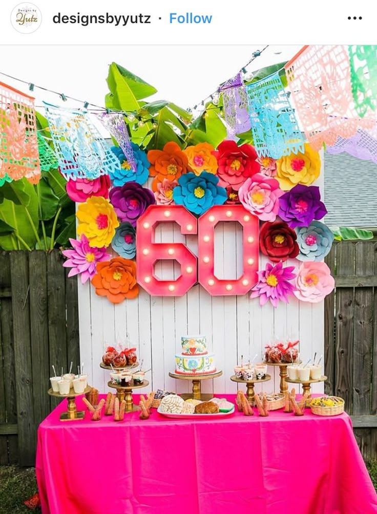 a table topped with lots of cake and cupcakes next to a neon sign