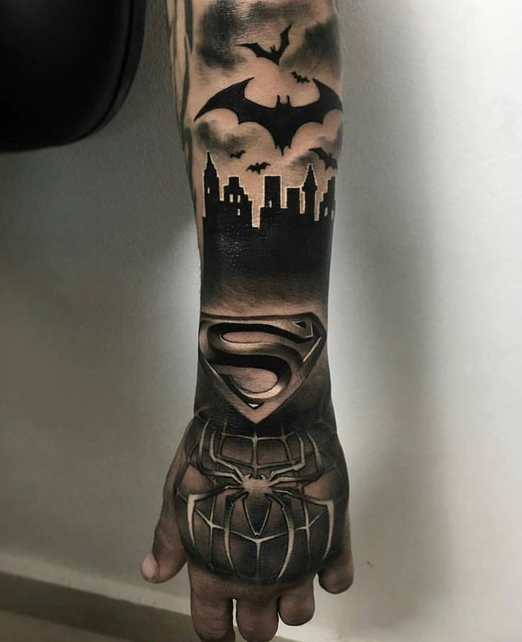 a man's arm with a batman and spider - man tattoo on the left hand