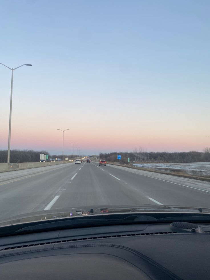 a view from the dashboard of a car driving down an empty highway at sunset or dawn