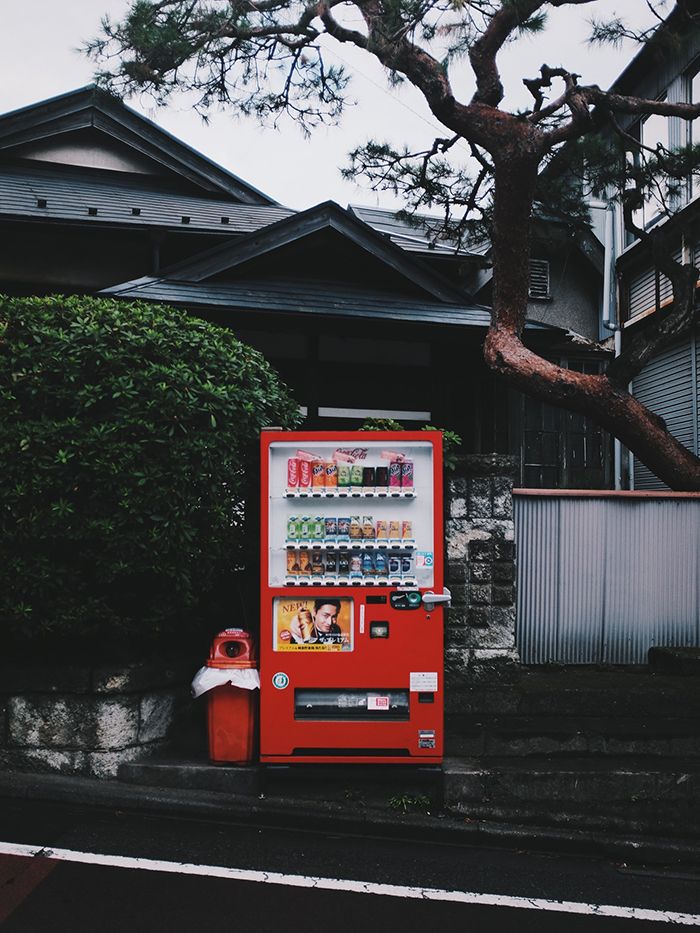 a red vending machine sitting on the side of a road next to a tree