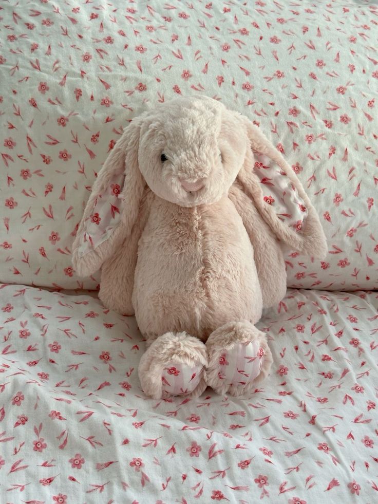 a stuffed animal sitting on top of a bed covered in pink and white sheets with red flowers