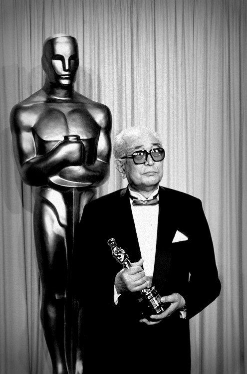 an older man in a tuxedo poses with his oscar statue