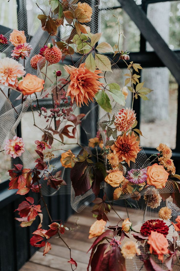 an arrangement of flowers hanging from the ceiling in front of a glass window with mesh netting