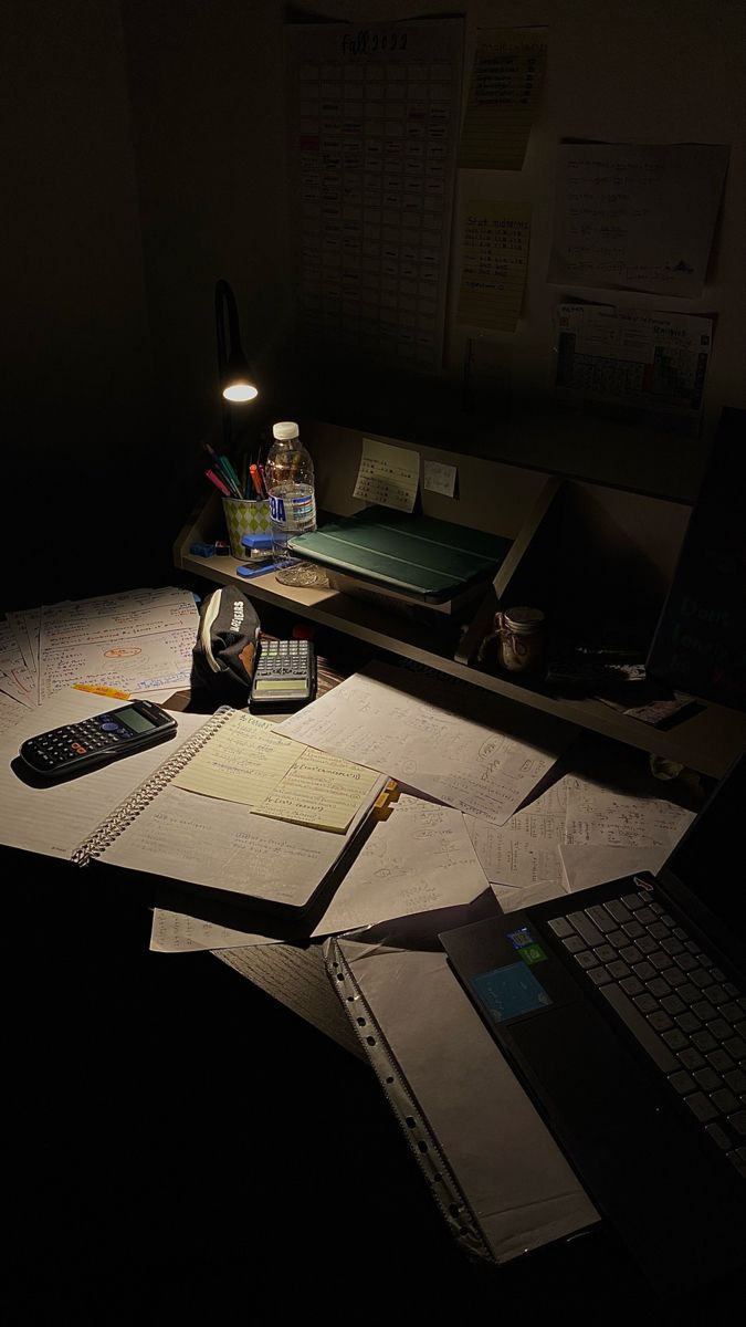 an office desk with notebooks, calculator and pen on it in the dark