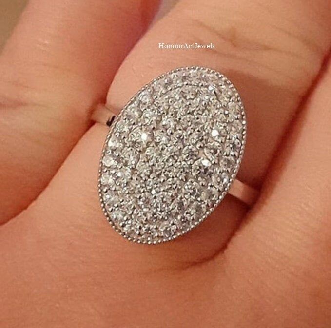 a woman's hand with a diamond ring on top of her finger and an oval shaped stone in the middle