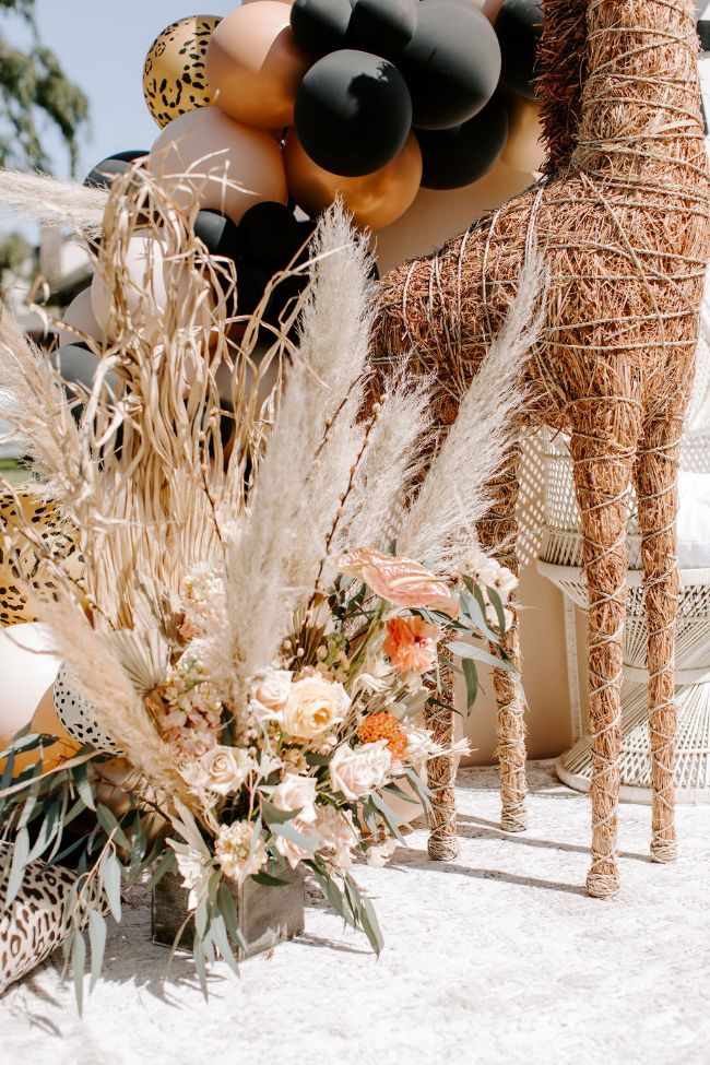 a giraffe is standing in the sand next to some flowers and balloons that look like zebras