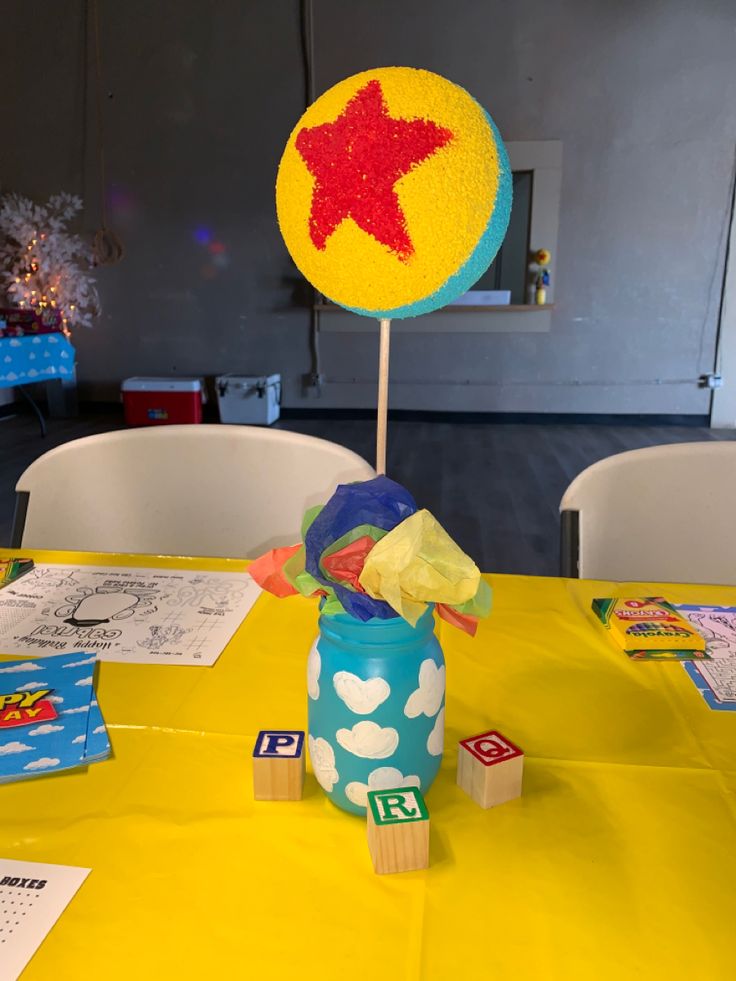 a yellow table topped with a blue vase filled with candy and a red star on top of it