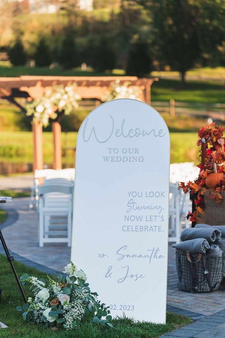 a welcome sign sitting on top of a grass covered field next to a white chair