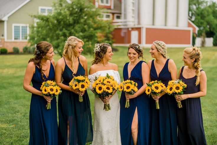 a group of women standing next to each other in front of a field with sunflowers