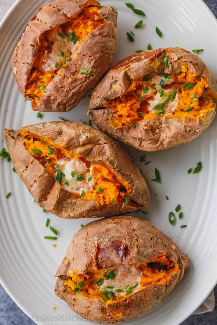 three baked potatoes on a white plate with green garnish