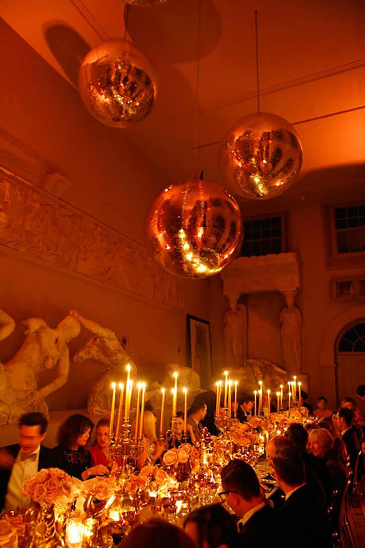 a group of people sitting around a dinner table with candles in front of them and disco balls hanging from the ceiling