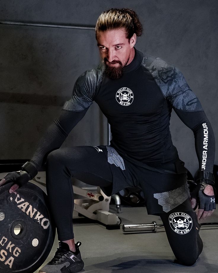 a man with a beard squatting on a barbell in a black shirt and leggings